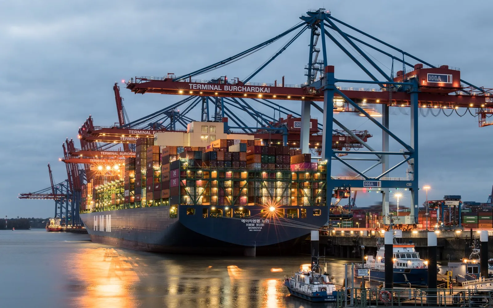 Container ship loaded with containers at a lit port terminal in the evening