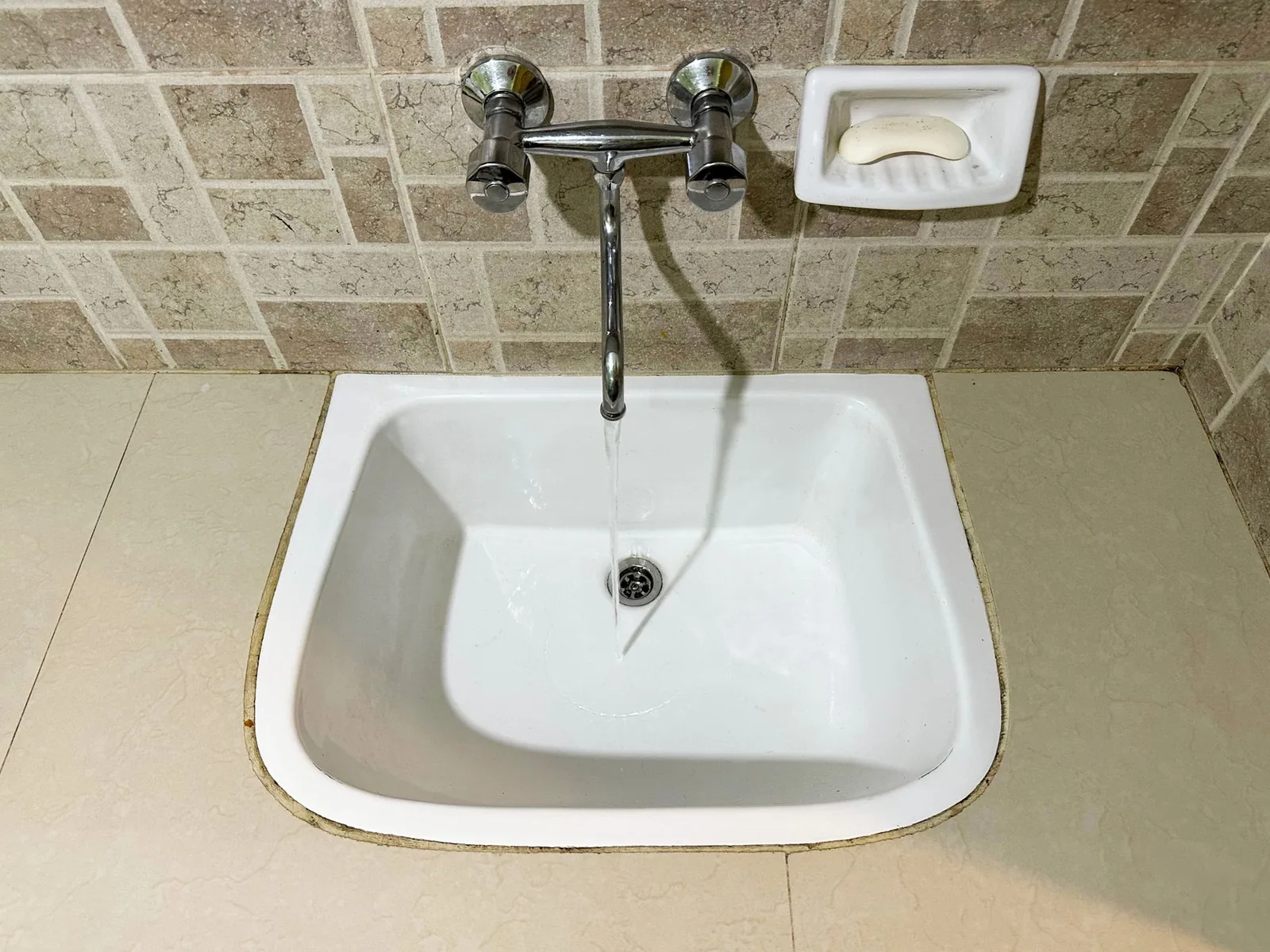 Plain bathroom sink with running water and a bar of soap in a wall soap dish