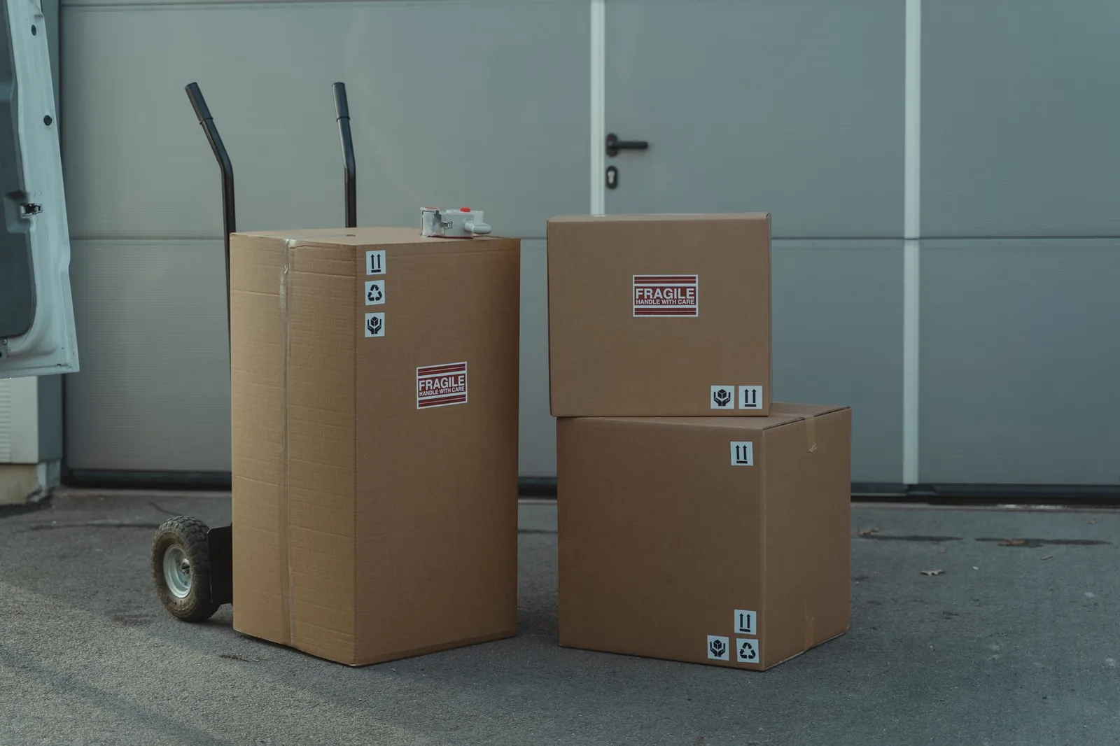 Two-wheel dolly beside three large cardboard boxes on a loading area